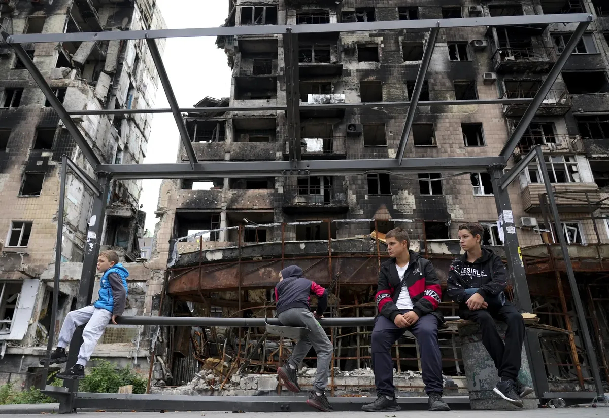 Children waiting at a destroyed bus stop in front of damaged buildings in Mariupol. Photo: Stringer / Anadolu Agency / Getty Images