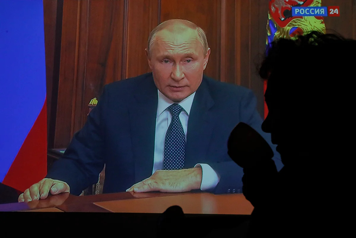 Женщина на фоне экрана телевизора, на котором Владимир Путин во время телеобращения к нации в Москве, Россия, 21 сентября 2022 года. Фото: Сергей Ильницкий / EPA