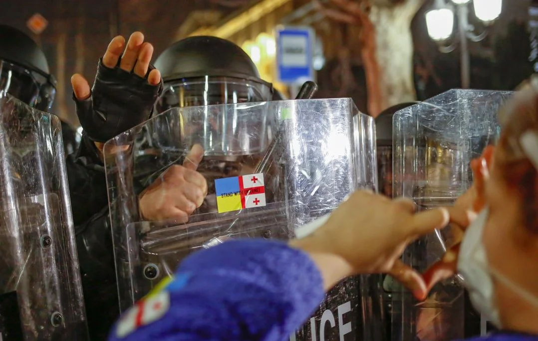 Участница протеста приклеивает на щит спецназовца флаги Украины и Грузии. Фото: Achi Gegenava / Instagram