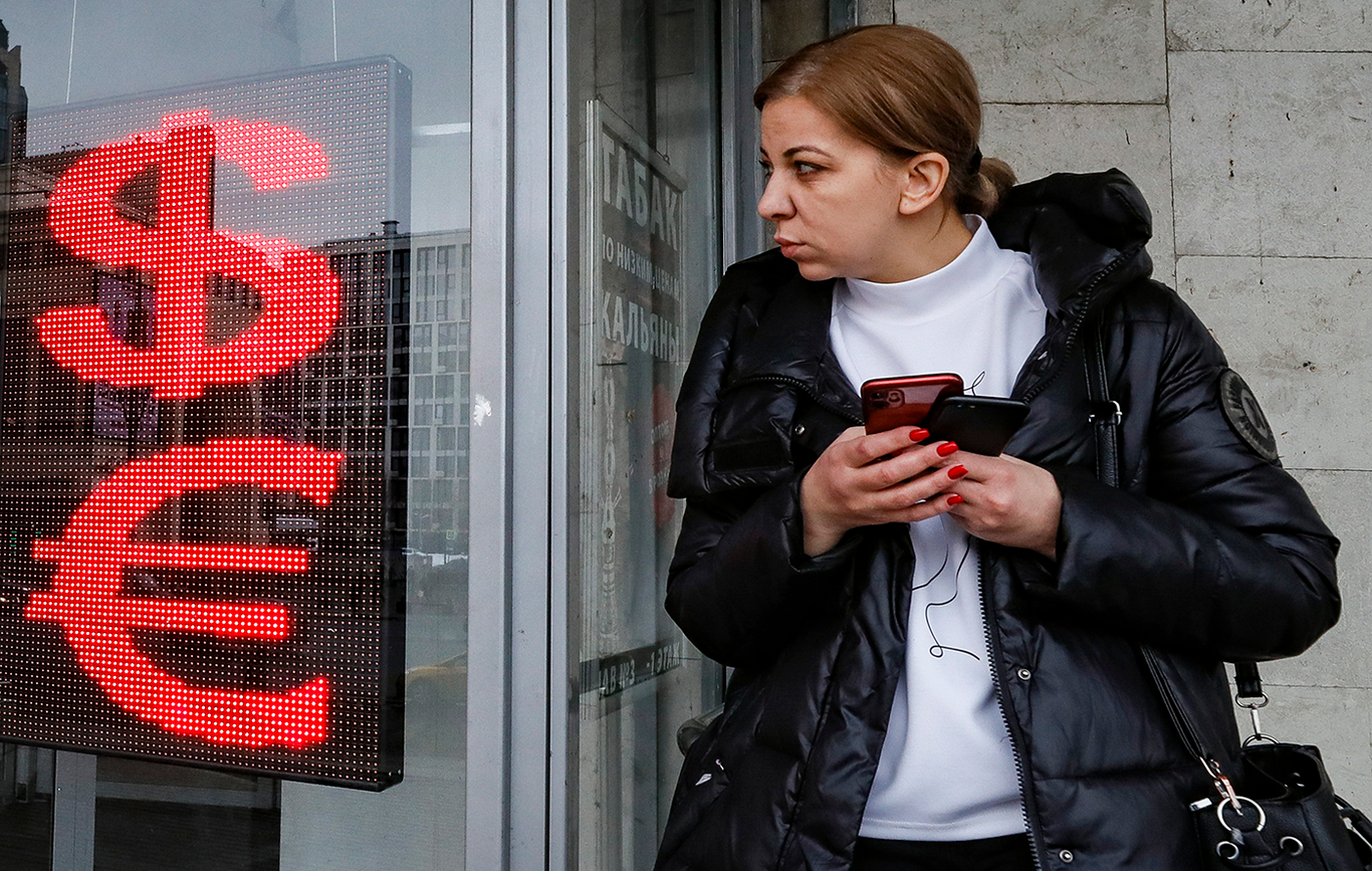 Женщина у изображений знаков евро и доллара в обменном пункте в Москве. Россия. 9 февраля 2023 года. Фото: Юрий Кочетков / EPA