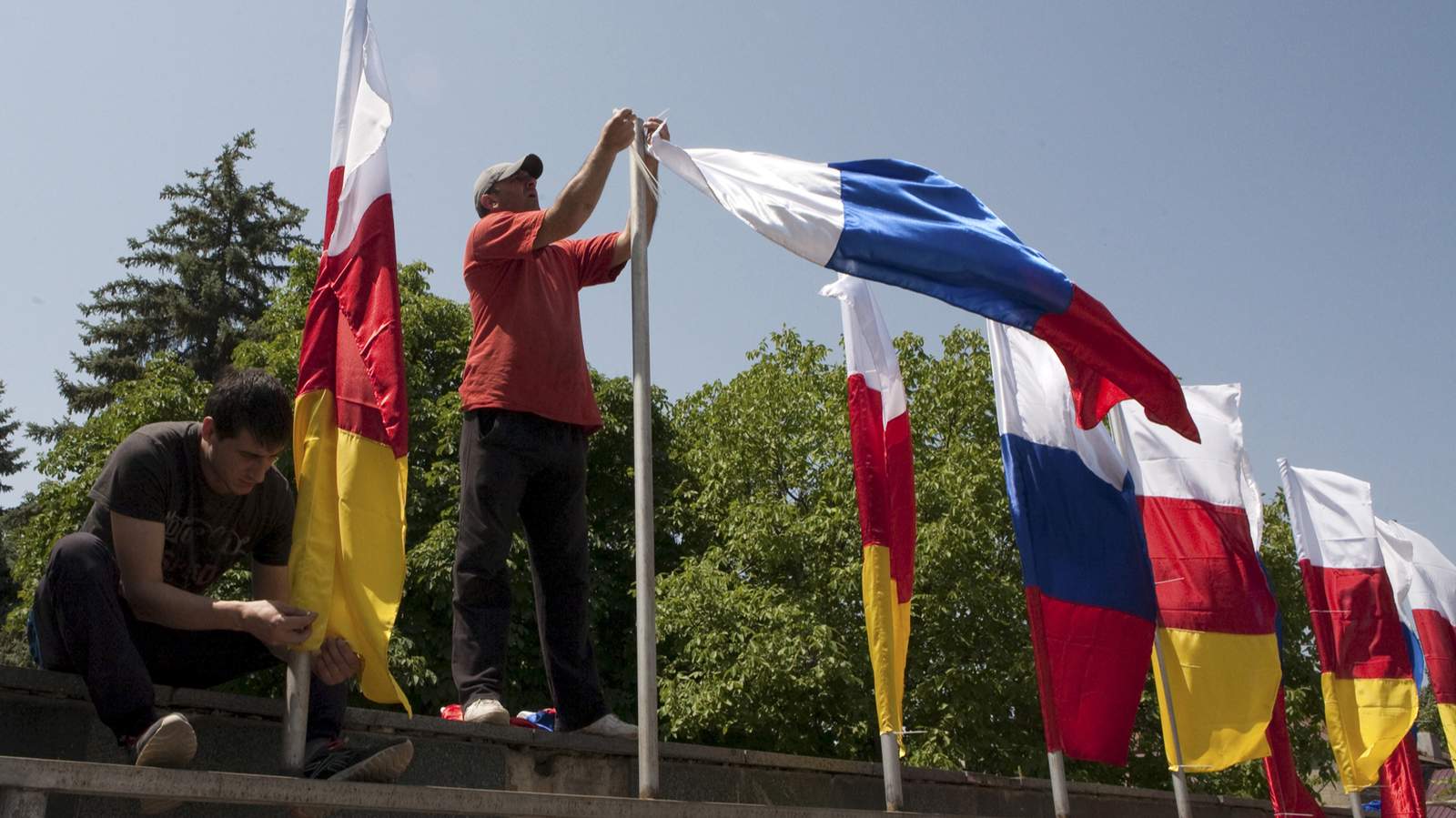 Мужчины закрепляют флаги Южной Осетии и России во время подготовки к церемонии принятия военной присяги в Цхинвале, Южная Осетия, 5 июля 2015 года. Фото: Kazbek Basaev / Reuters / Scanpix / LETA<br>