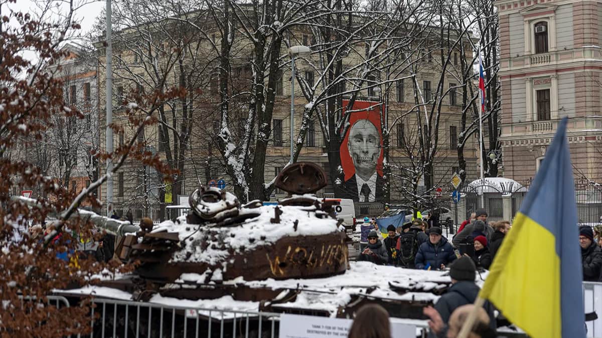 Сгоревший российский танк, привезенный из Украины на фоне иллюстрации с изображением Владимира Путина у российского посольства в Риге, 24 февраля 2023 года. Фото: Владислав Докшин / «Новая-Европа»