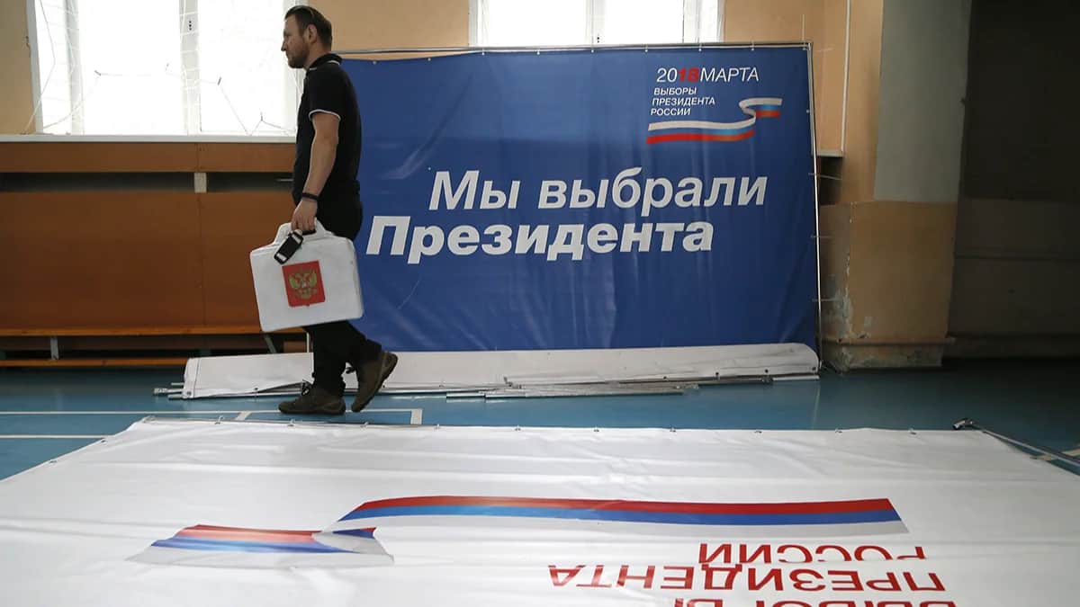 Член участковой избирательной комиссии идет рядом с баннером с надписью «Мы выбрали президента» во время подготовки к президентским выборам в Москве, 16 марта 2018 года. Фото: Максим Шипенков / EPA-EFE