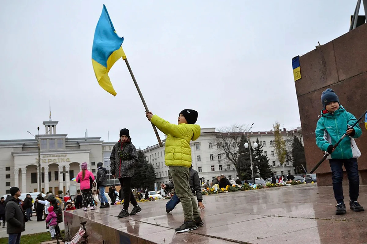 Дети машут украинскими флагами на главной площади Херсона после освобождения города украинскими военными, Украина, 13 ноября 2022 года. Фото: Иван Антипенко / EPA-EFE (edited) 