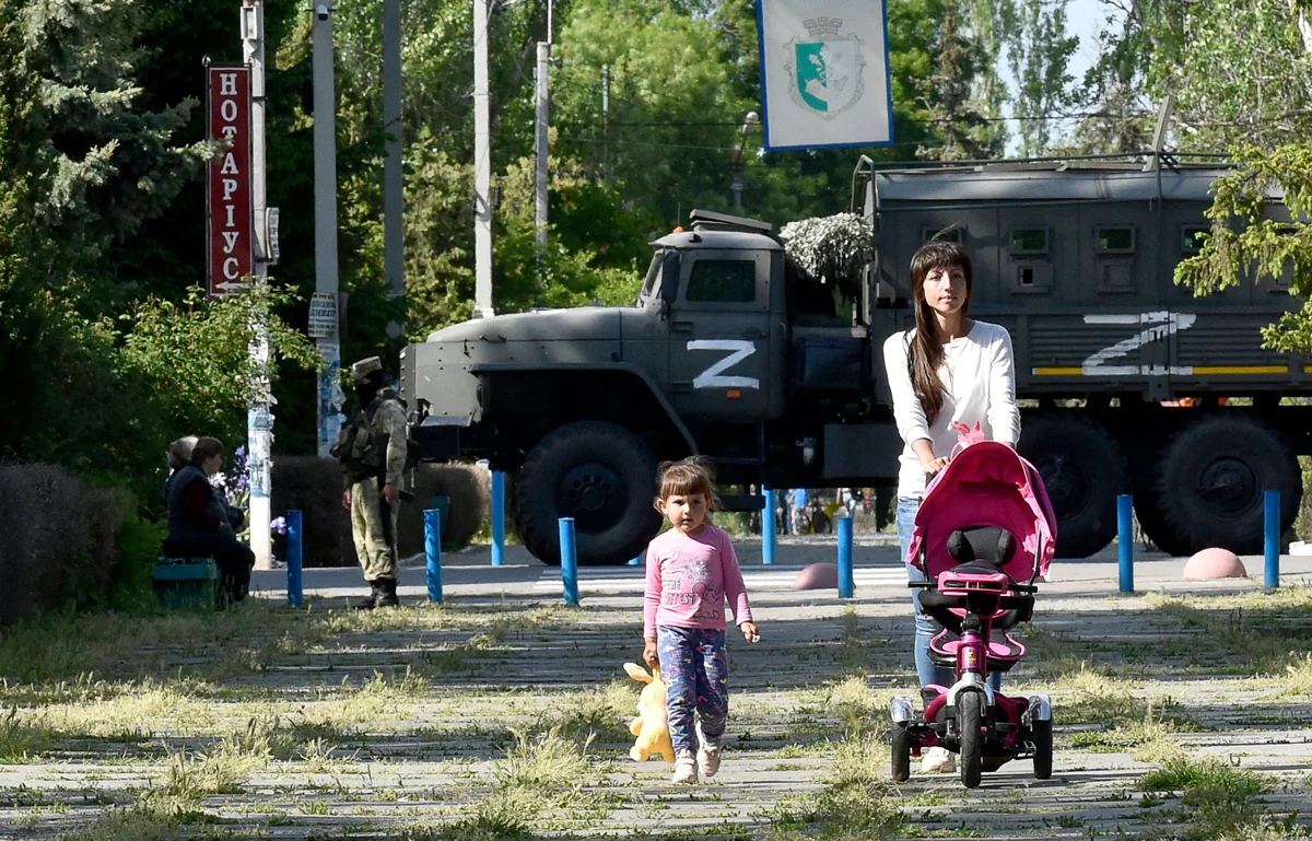 Женщина с ребенком на фоне российских военных в приморском Скадовске, Запорожская область, 20 мая 2022 года. Фото: Ольга Мальцева / AFP / Scanpix / LETA