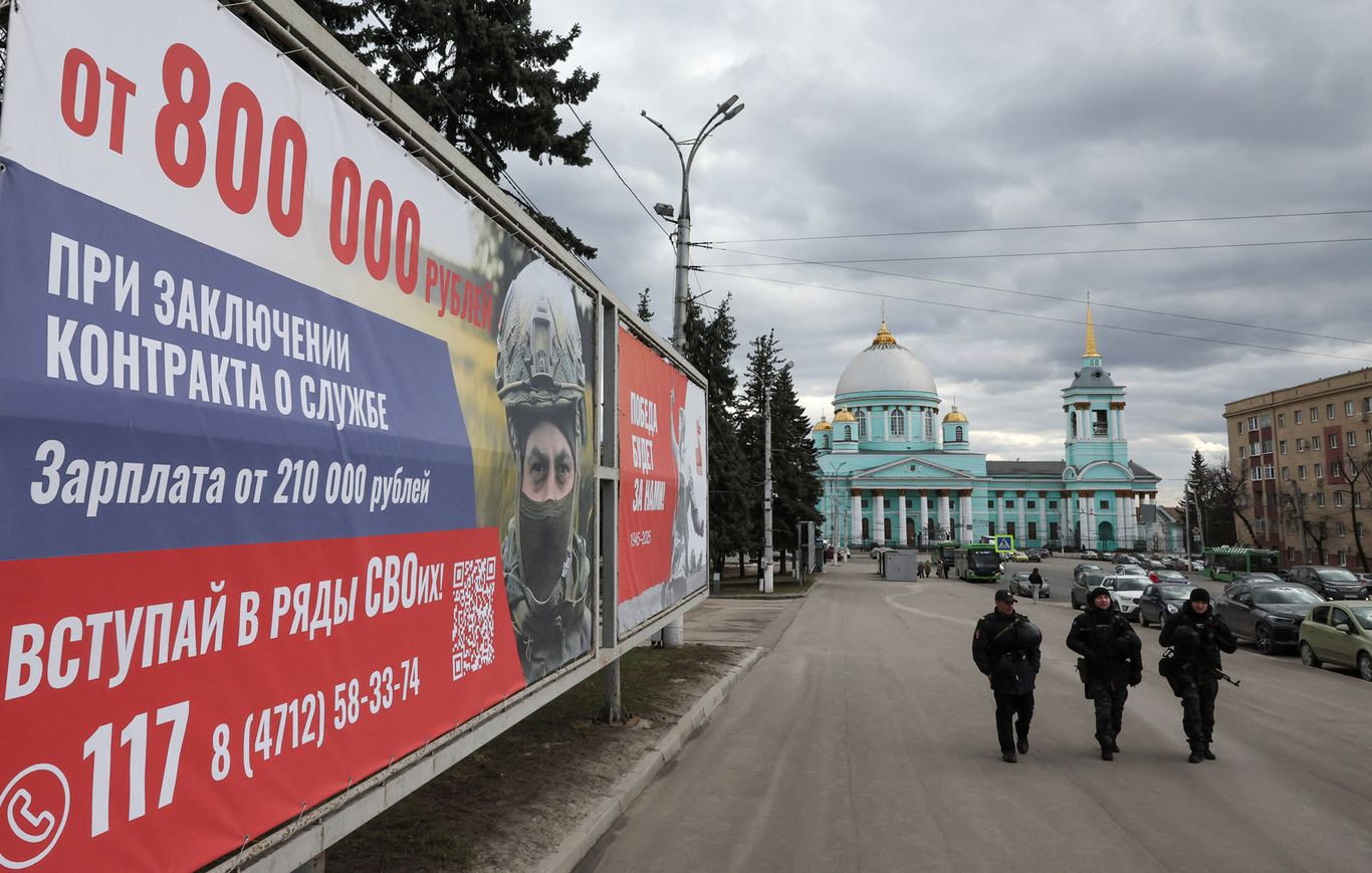 Вооруженные сотрудники правоохранительных органов патрулируют улицу и проходят мимо плаката с рекламой службы по контракту. Курск. 20 марта 2025 года. Фото: Шамиль Жуматов / Reuters / Scanpix / LETA
