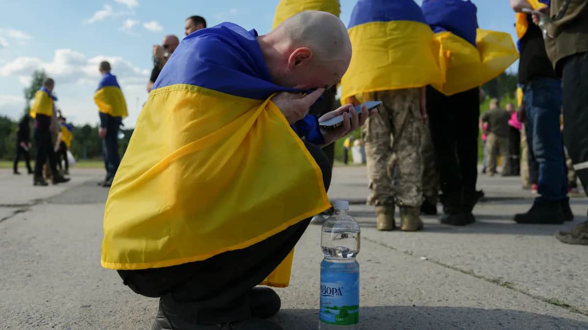 A Ukrainian prisoner wrapped in his national flag makes an emotional phone call following his release from captivity in Russia, 23 May 2025. Photo: EPA
