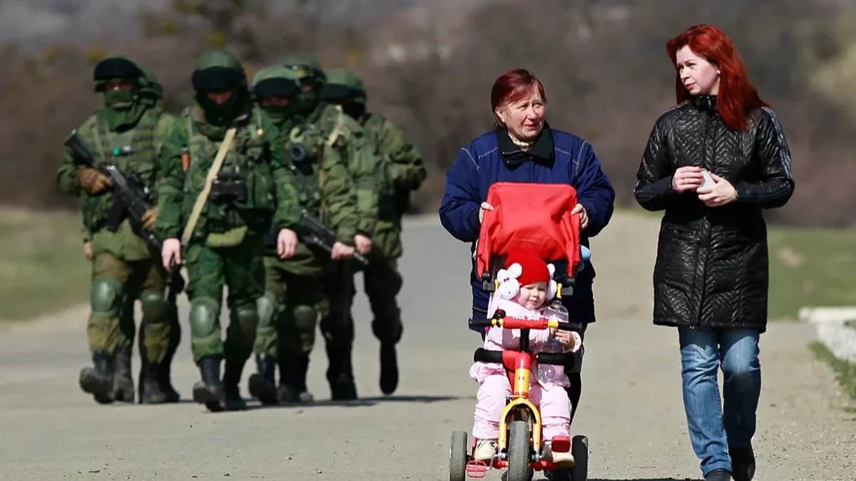 Women walk on the road in front of armed men in military uniform seen outside a Ukrainian military base near Simferopol, 14 March 2014. Photo: EPA/YURI KOCHETKOV