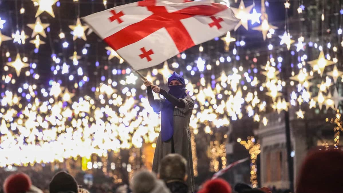 Участница оппозиционного митинга перед зданием парламента держит флаг Грузии в Тбилиси, 22 декабря 2024 года. Фото: David Mdzinarishvili / EPA