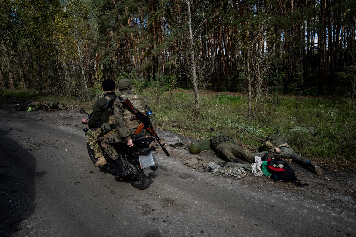 Украинские военные проезжают на мотоцикле мимо тел российских военнослужащих в городе Лиман, Украина, 3 октября 2022 года. Фото: Евгений Малолетка / AP Photo / Scanpix / LETA