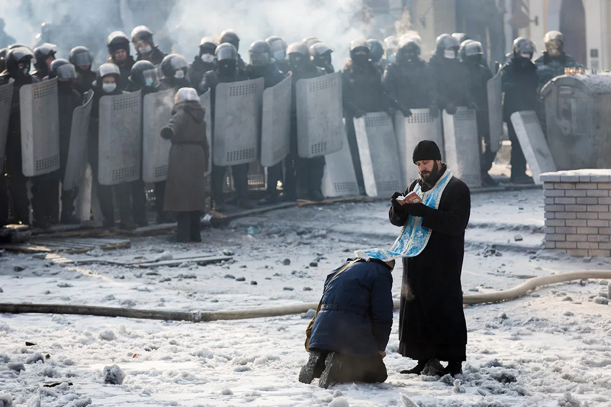 A man kneeling before an Orthodox priest between the police and anti-government protesters near the Dynamo Stadium, Kyiv, 25 January 2014. Photo: Rob Stothard / Getty Images