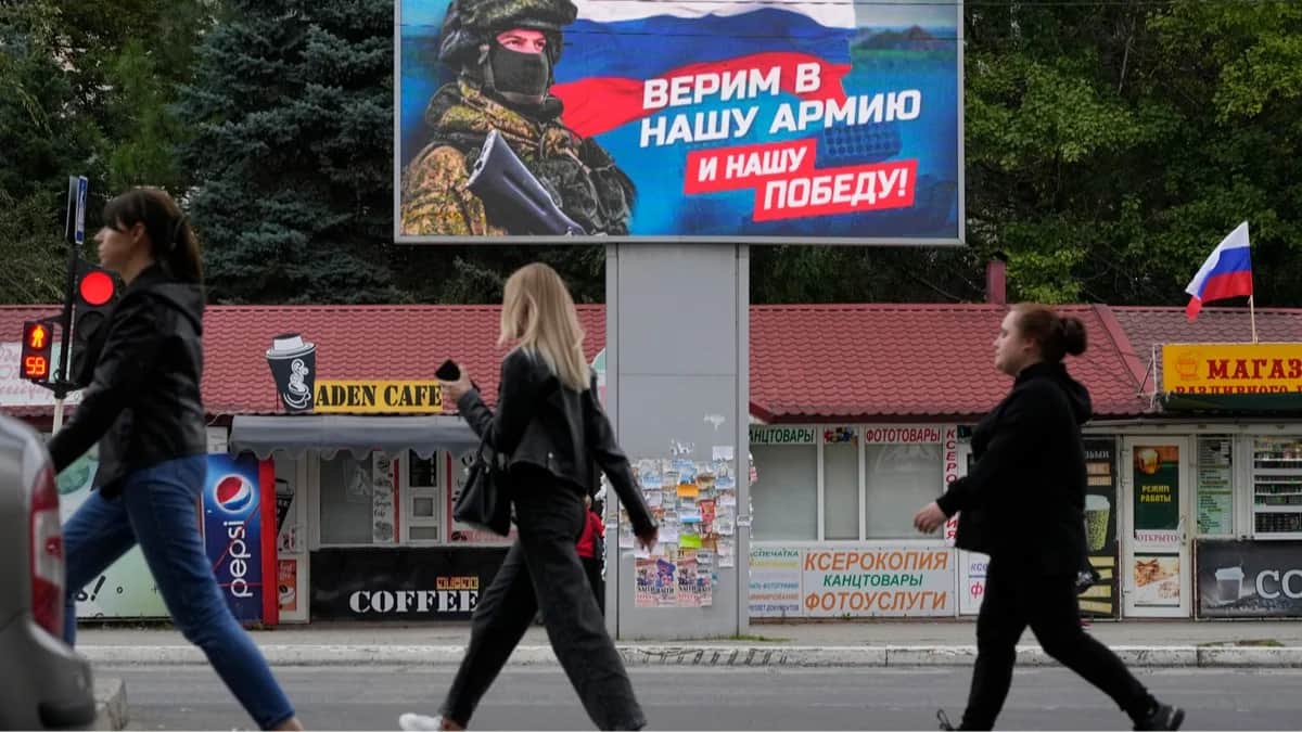 Люди проходят мимо баннера с изображением военнослужащего и флага России в Луганске, Луганская область, Украина, 27 сентября 2022 года. Фото: AP Photo / Scanpix / LETA<br>